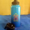 Kinnikinnick Trading Co. Water Bottle Blue water bottle with black cap and strap on blue surface against yellow wall.