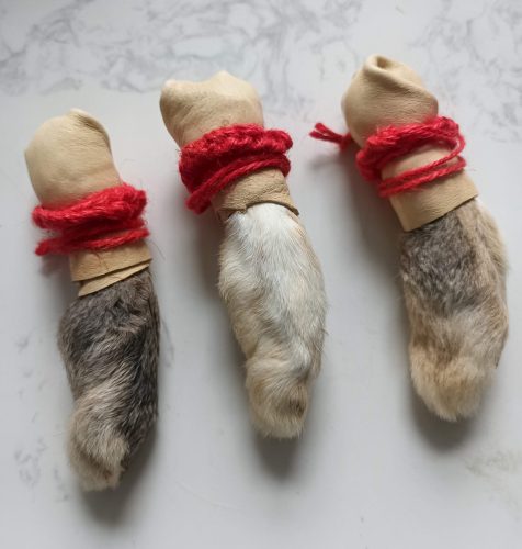 Three lucky rabbit foot charms with red yarn and paper bandages on a white surface.